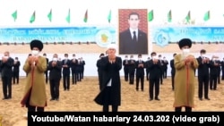 Туркменские старейшины и чиновники на фоне изображения президента Сердара Бердымухамедова, который занял пост в марте 2022 года вместо отца. Портреты Сердара и Гурбангулы Бердымухамедовых висят повсюду, их нет "разве что в туалетах"