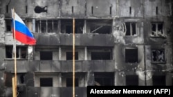 Российский флаг на фоне сгоревшего здания в оккупированном после блокады Мариуполе, апрель 2022 года