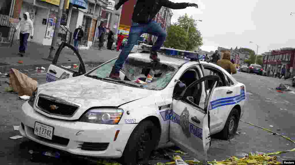 Один из участников уличных беспорядков в Балтиморе на поврежденной полицейской машине 