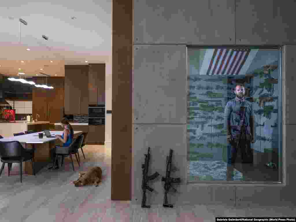 Роберт Болдвин-младший в оружейной комнате в своем доме в Лас-Вегасе (16 апреля 2019). За столом работает его девушка. Первое оружие – винтовку 22-го калибра – ему подарил отец, когда Роберту было 6 лет. Первое место в категории "Портрет, фоторепортаж", автор – Габриэль Галимберти