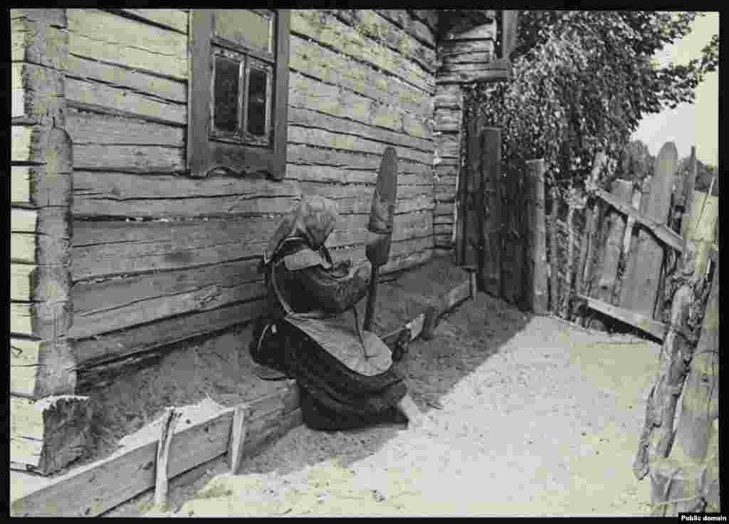 Женщина прядет во дворе своей хаты   