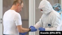 Специалист в защитном костюме помогает президенту России Владимиру Путину снять защитные перчатки во время посещения больницы для пациентов с подозрением на заболевание COVID-19 в поселке Коммунарка в Новой Москве, Россия, 24 марта 2020 года